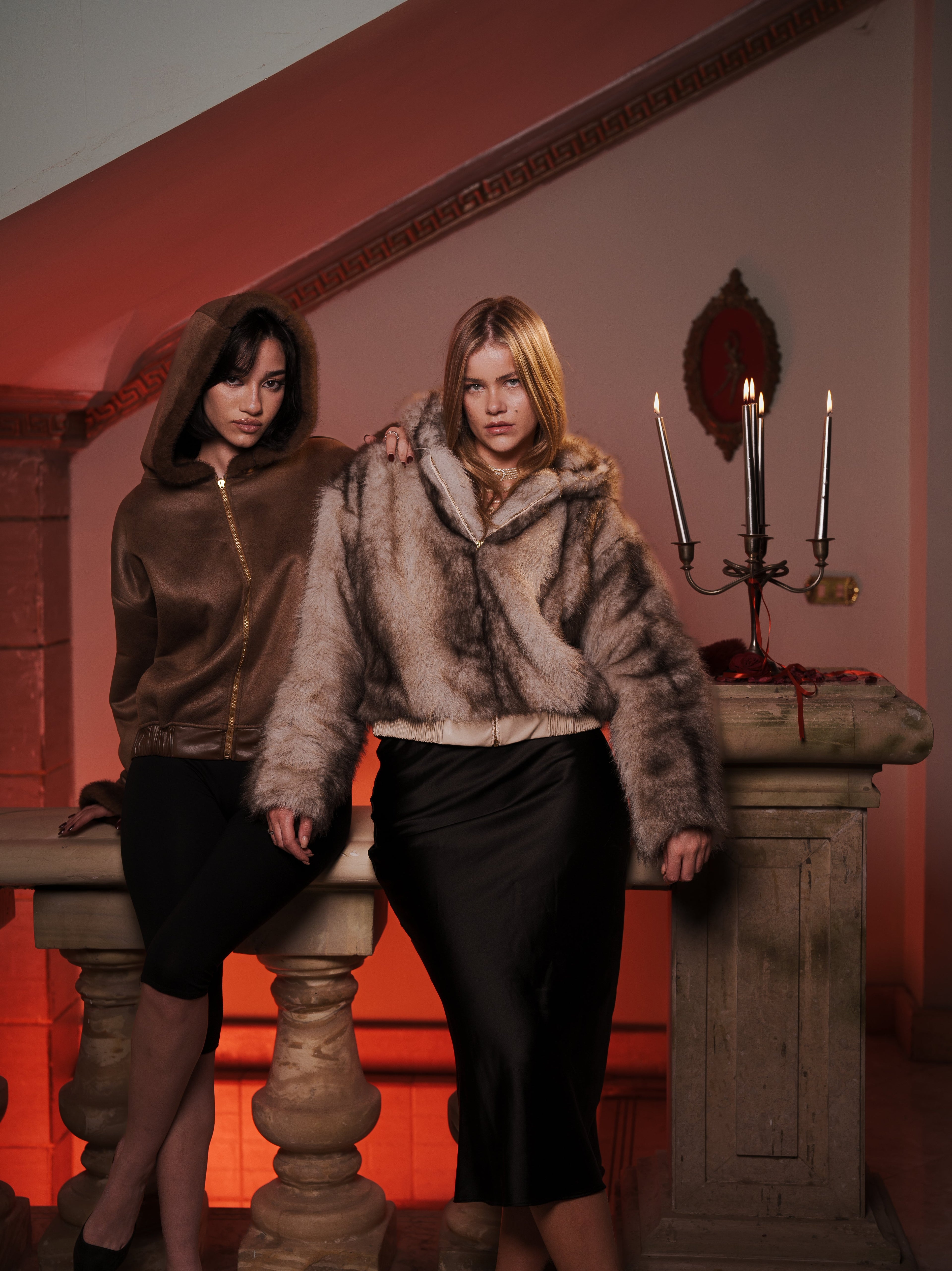 Two women wearing reversible brown faux fur and suede jackets from the Chemate collection, standing in a warm, candle-lit setting that highlights modern femininity and modest fashion.